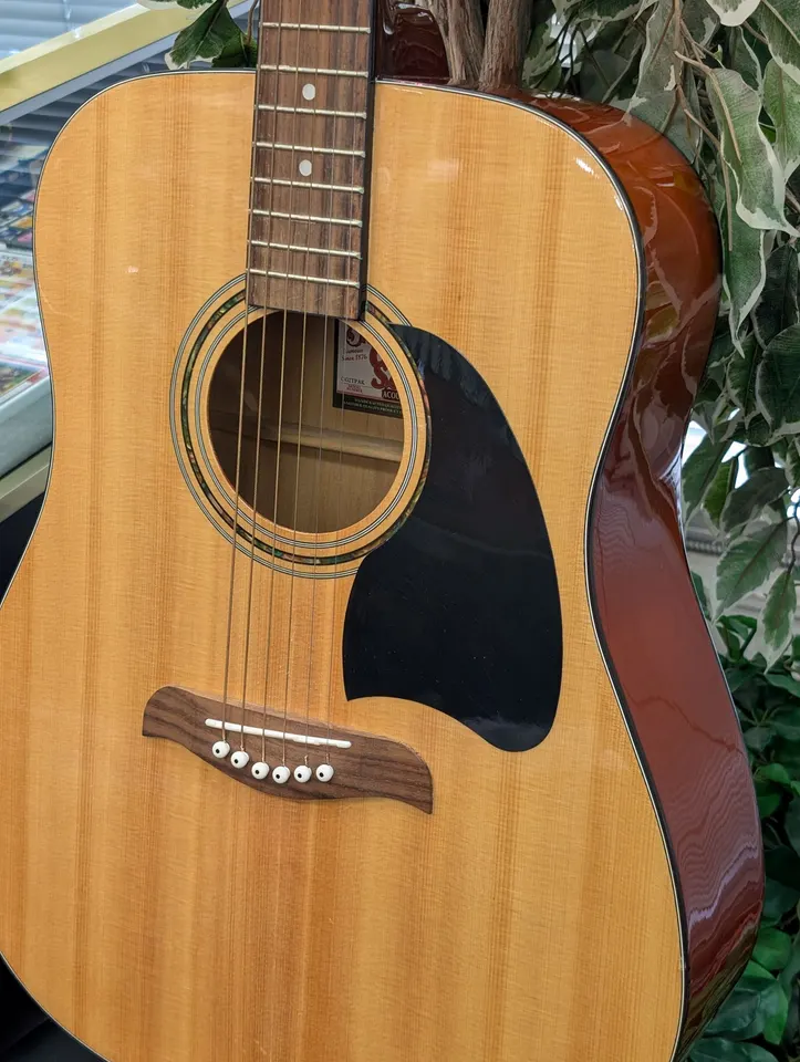 Natural Oscar Schmidt by Washburn OG2TPAK dreadnought acoustic guitar showing its spruce top, black pickguard, rosewood bridg