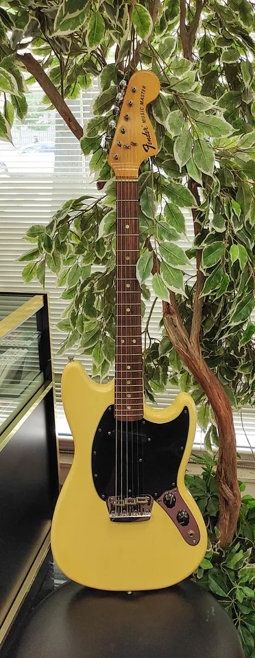 Vintage 1976 Fender Musicmaster electric guitar in naturally aged cream-yellow white finish with black pickguard, rosewood