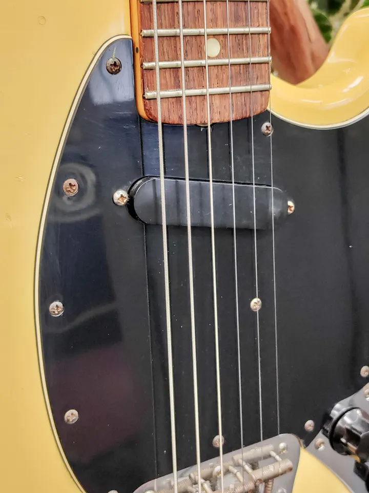 Vintage 1976 Fender Musicmaster electric guitar in naturally aged cream-yellow white finish with black pickguard, rosewood