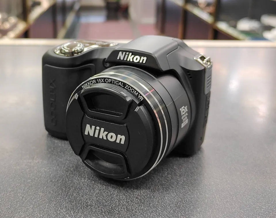 Nikon COOLPIX L100 black digital camera shown from multiple angles with lens cap, pop-up flash, LCD screen, battery sd card